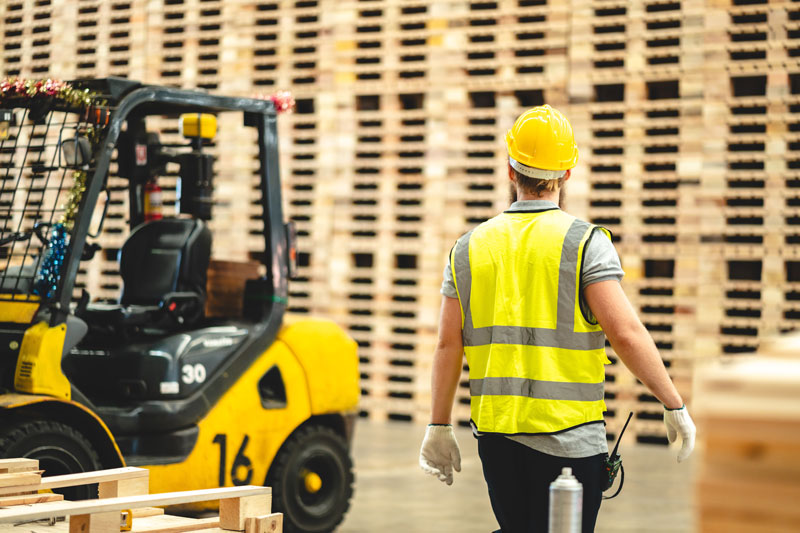 Worker in yellow vest near a forklift and wall of pallets